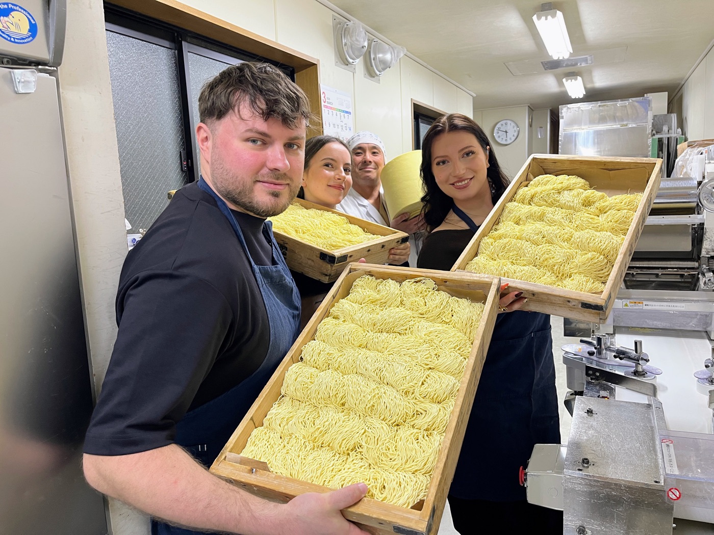 Guests smiling and holding wooden trays filled with the noodles they made