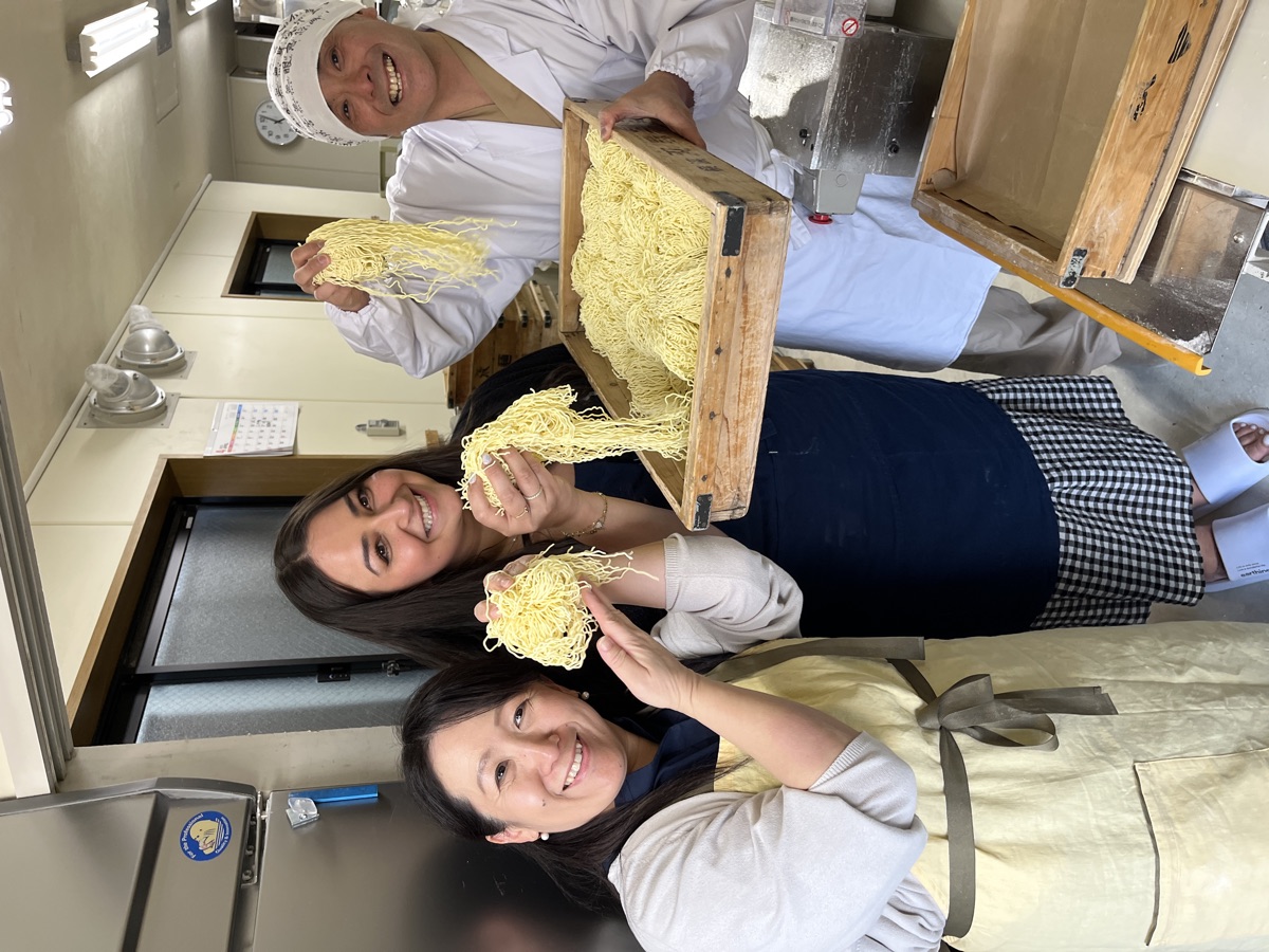 Akiko, a guest and Taka laughing while holding up freshly made ramen noodles