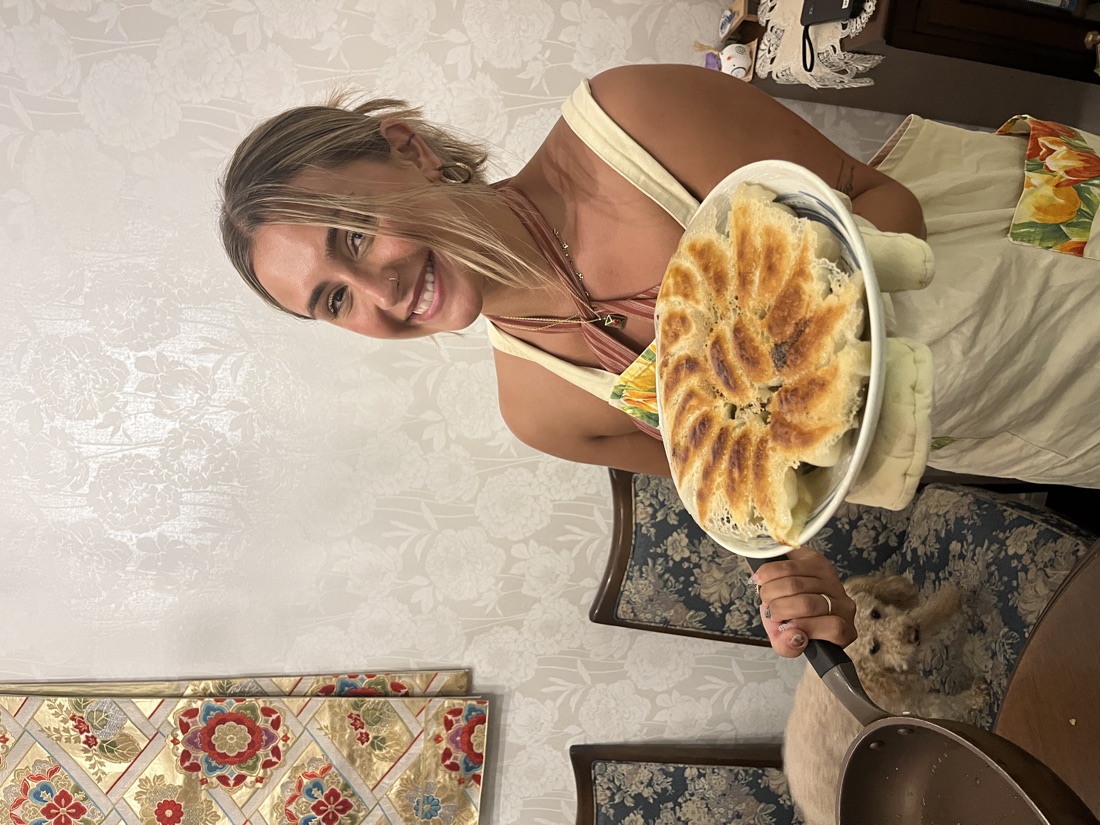 A guest presenting a plate of golden pan-fried gyoza fresh from the pan