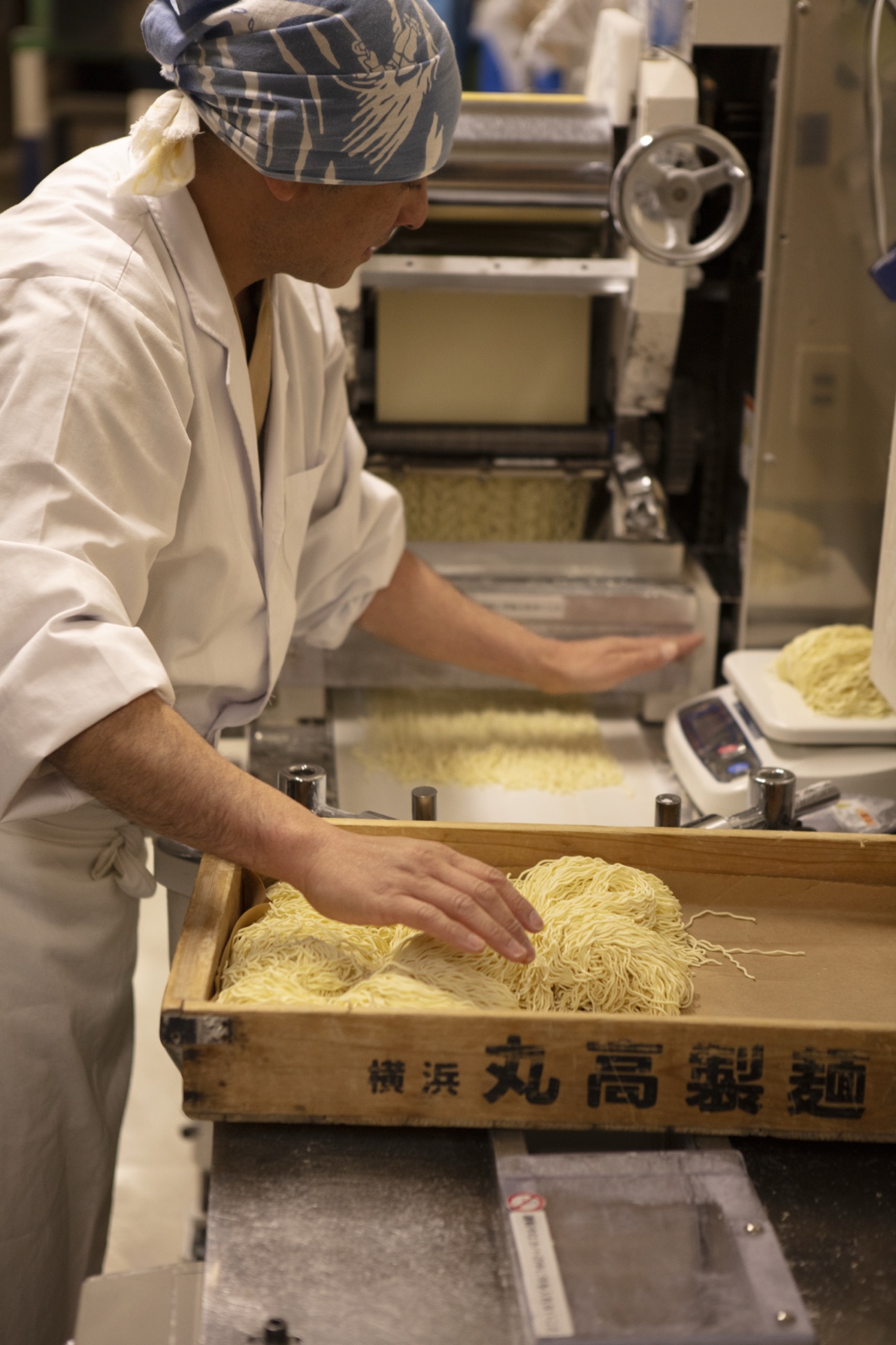 Taka in his white work coat gathering freshly cut ramen noodles into a wooden Marutaka Seimen box